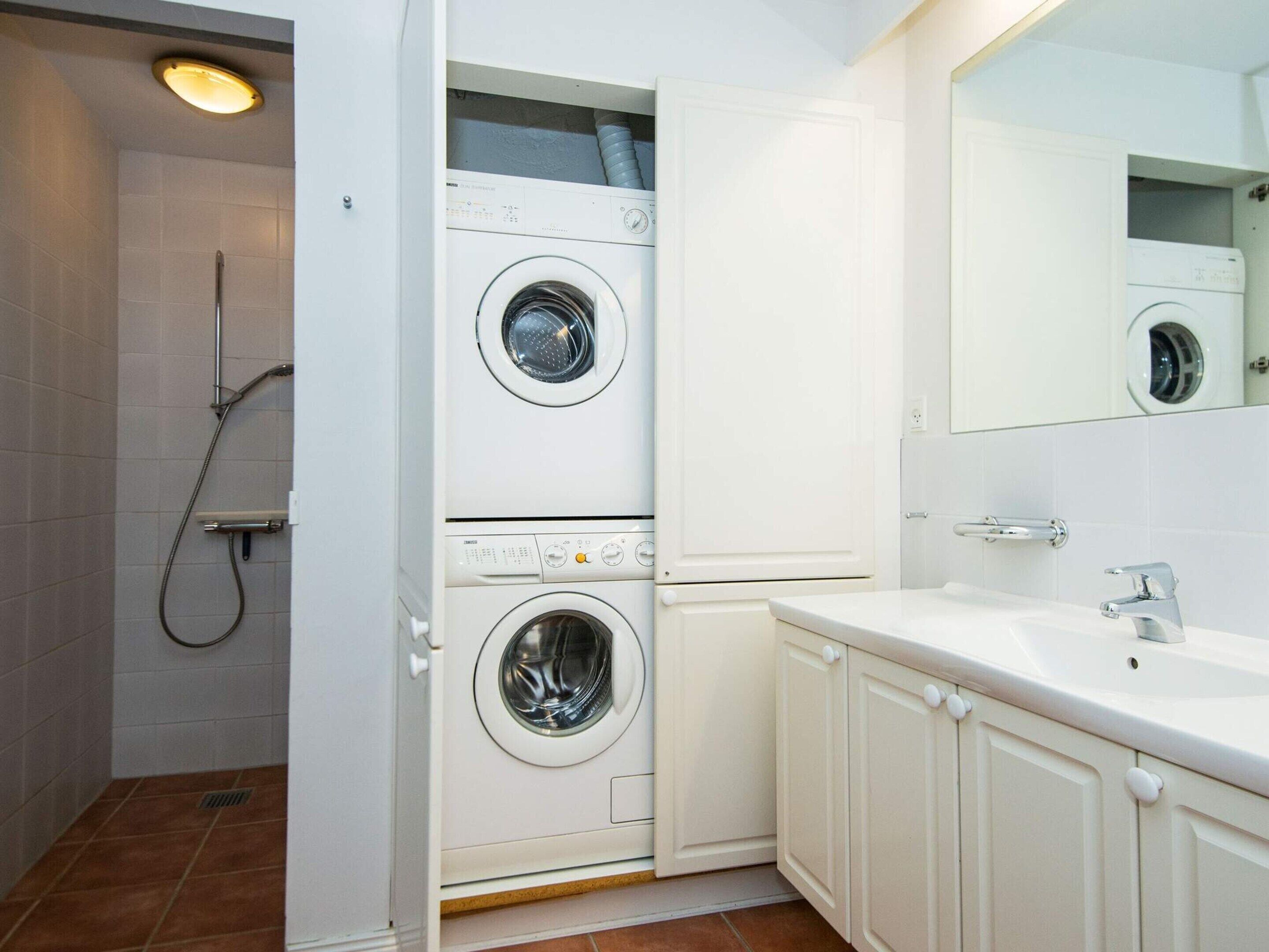 A laundry room with two washing machines, a shower, and a sink with a mirror.