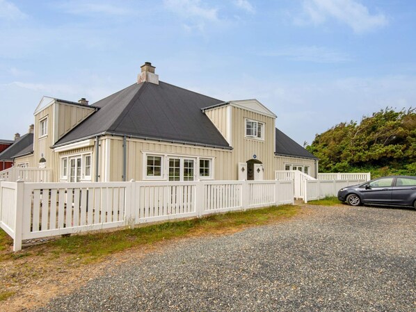 Een twee verdiepingen tellend huis met een witte picket fence, een grindpad en een geparkeerde auto.