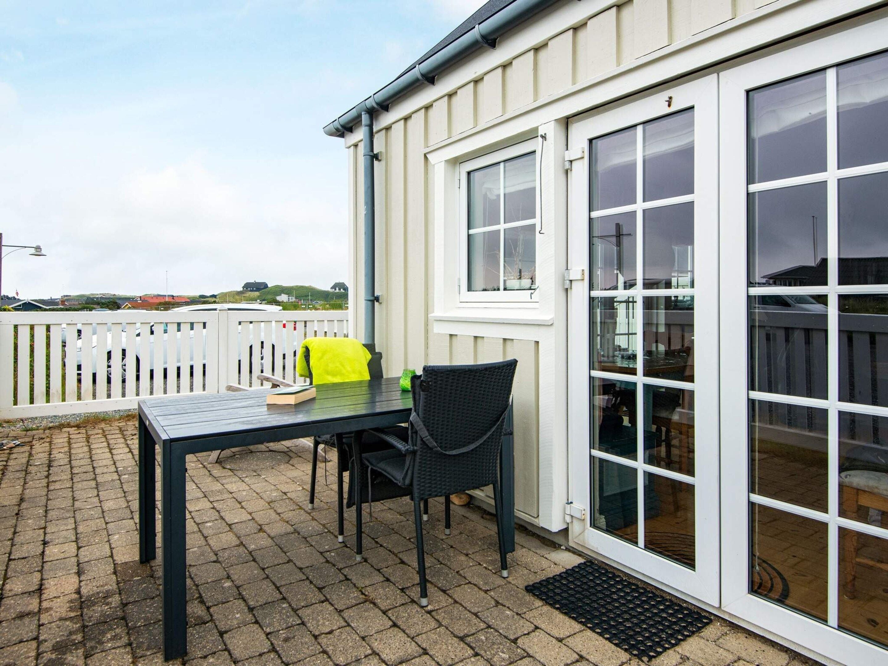 An outdoor patio with a table and chairs, a white fence, and a view of the landscape.