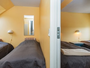 A hotel room with two single beds, a mirror, bedside lamps, and a door.