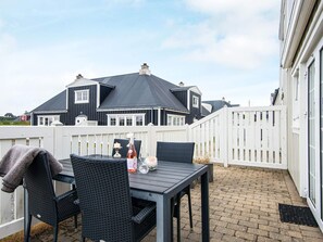 An outdoor patio with a table and chairs, a white fence, and a house with a dark roof in the background. - 4 Person Holiday Home in Ringkobing (Ringkobing)