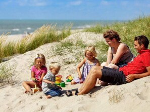 A family of four on a sandy beach with dunes and ocean in the background.