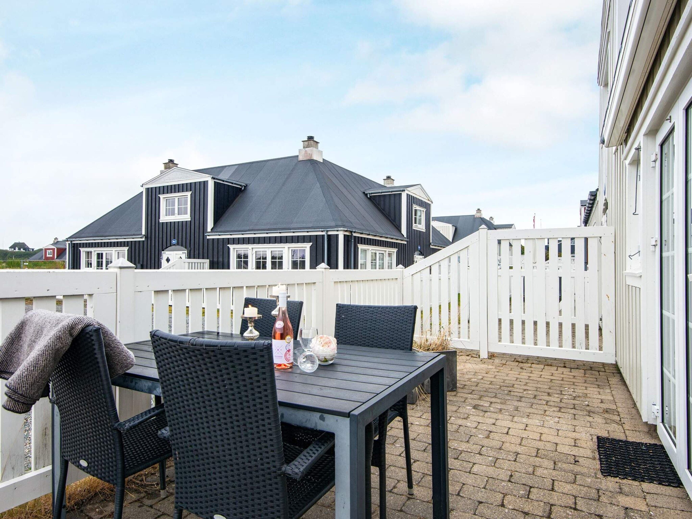 An outdoor patio with a table and chairs, a white fence, and a house in the background.