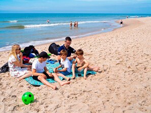 Een groep mensen zit op een strandlaken, met een groene voetbal in de buurt.