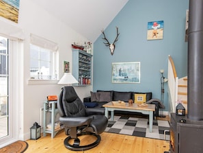 Een knus woongedeelte met een open haard, een comfortabele bank, een eettafel en een boekenplank.
