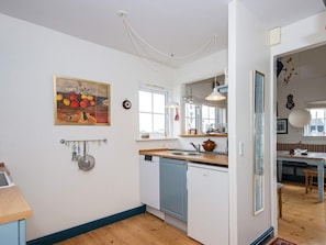 A kitchen with a window, a sink, a refrigerator, and a painting on the wall.