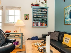 Een gezellige woonkamer met een boekenkast, een lamp, een bijzettafeltje met lekkernijen en een bank.