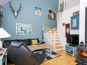 Ein Wohnzimmer mit einer Couch, einem Couchtisch, einem Kamin, einer Treppe und Wandbildern.