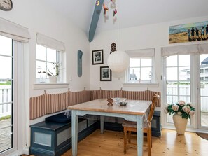 Una habitación con una mesa de madera, un banco con asientos a rayas, un ventanal y una puerta que da al exterior.