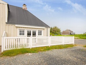 A house with a white picket fence, a grey roof, and a thatched-roof building in the background.