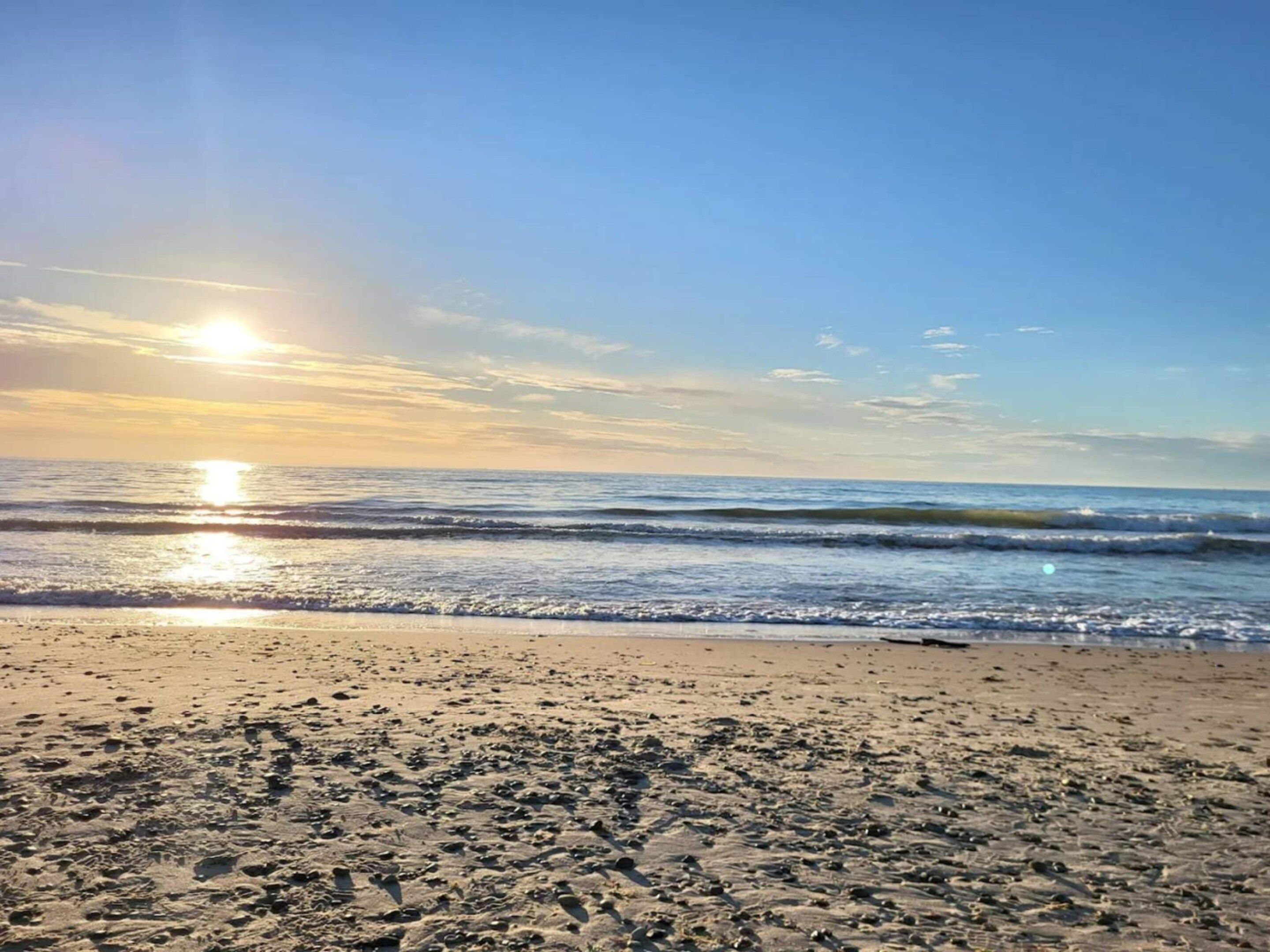 Une plage avec des vagues, un ciel dégagé et le soleil se couchant ou se levant.
