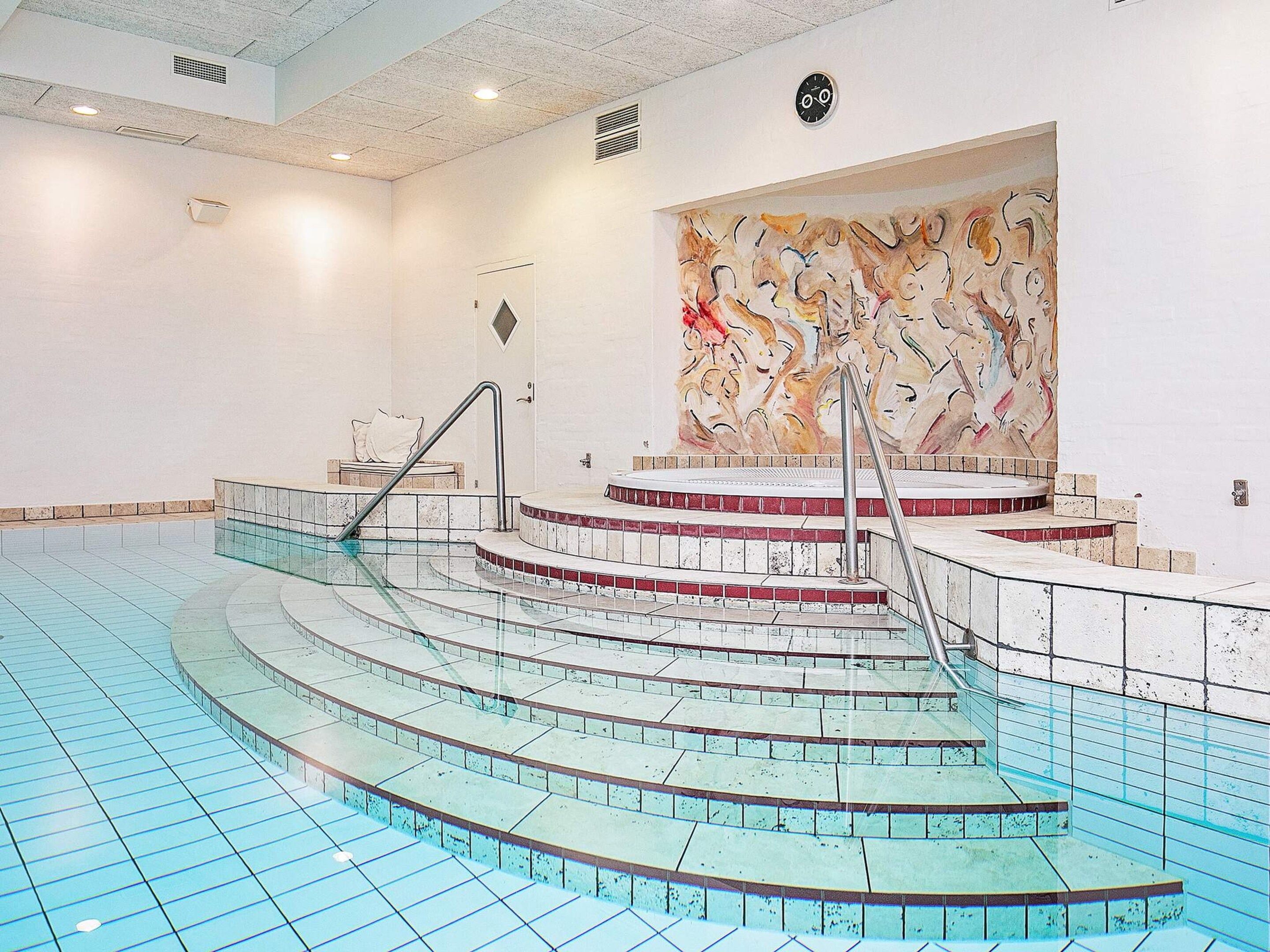 A swimming pool with a circular design, a staircase leading to a hot tub, and a large abstract painting on the wall.