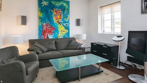 A modern living room with a sofa, a glass coffee table, a TV, and a large abstract painting on the wall. - 4 Star Holiday Home in Skagen (Skagen)