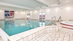 An indoor swimming pool with a tiled floor, a hot tub, and a seating area with chairs.