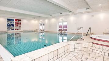 An indoor swimming pool with a tiled floor, a hot tub, and a seating area with chairs.