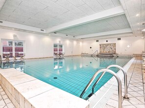 An indoor swimming pool with clear water, tiled walls, and a ceiling with recessed lighting.