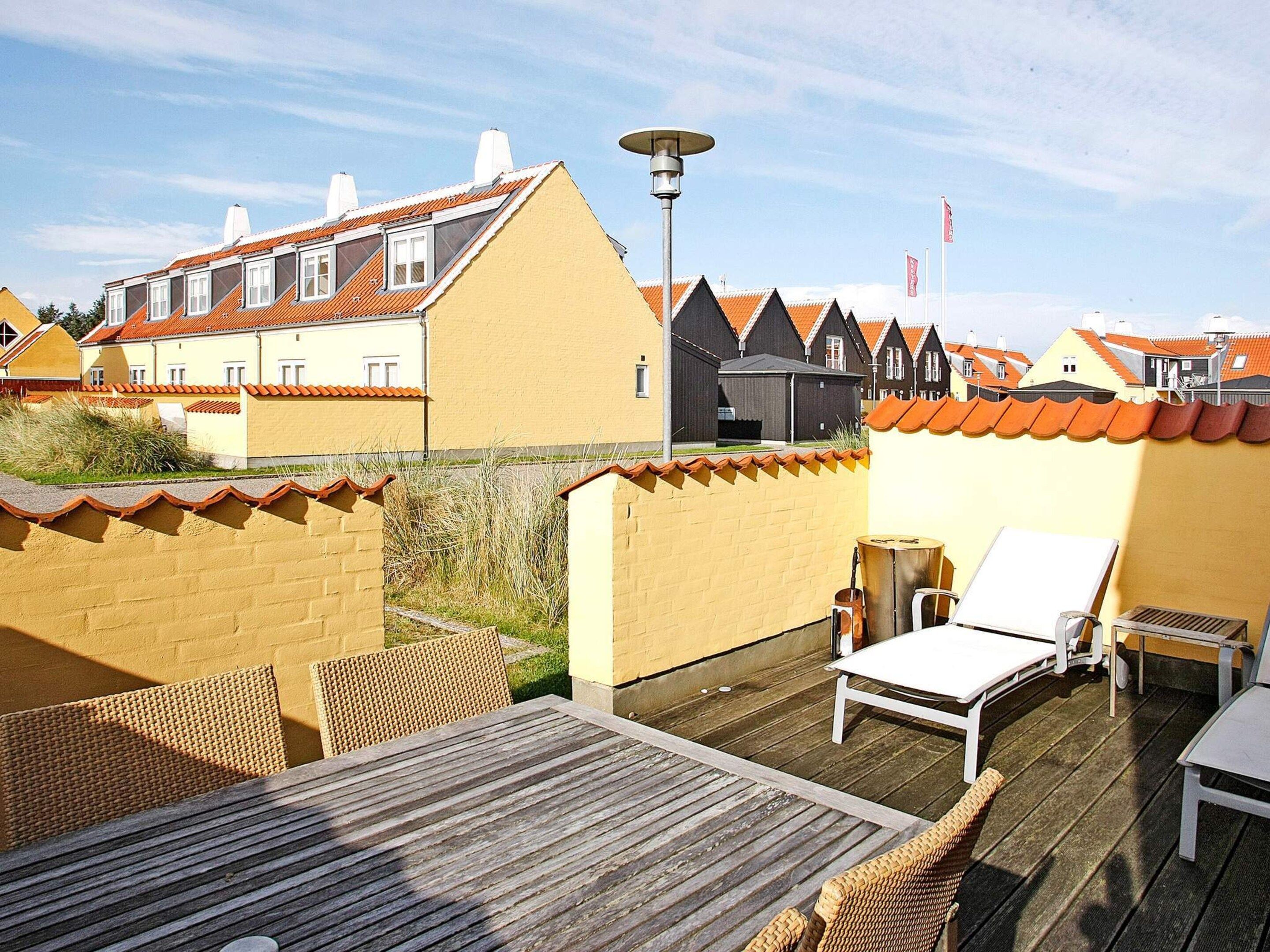 A rooftop terrace with a table, chairs, and a lamp.
