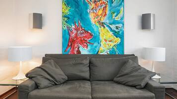 En moderne stue med en grå sofa, to væglamper og et farverigt abstrakt billede på væggen.