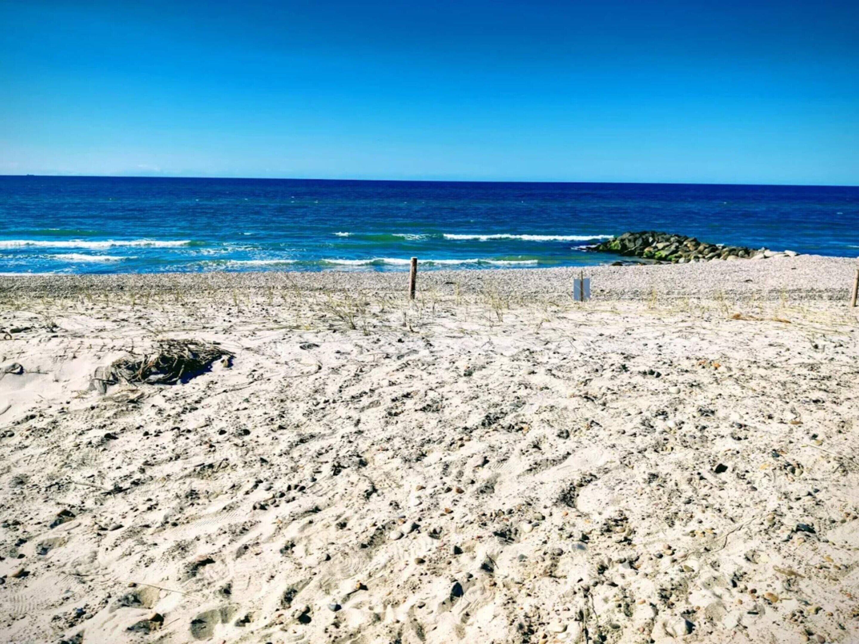 A beach with a clear view of the ocean, sandy terrain, and some rocks.