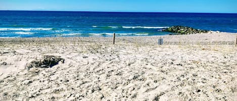 A beach with a clear view of the ocean, sandy terrain, and some rocks.