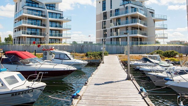 A marina with modern apartment buildings, boats docked, and a wooden walkway.