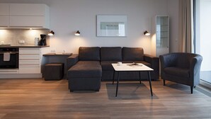 A modern living room with a sofa, a coffee table, and a chair. There is a kitchen area with cabinets and a coffee machine. - 5 Star Holiday Home in Wendtorf (Wendtorf)