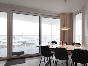 Uma sala de jantar com uma janela grande, uma mesa posta para quatro pessoas e um lustre.