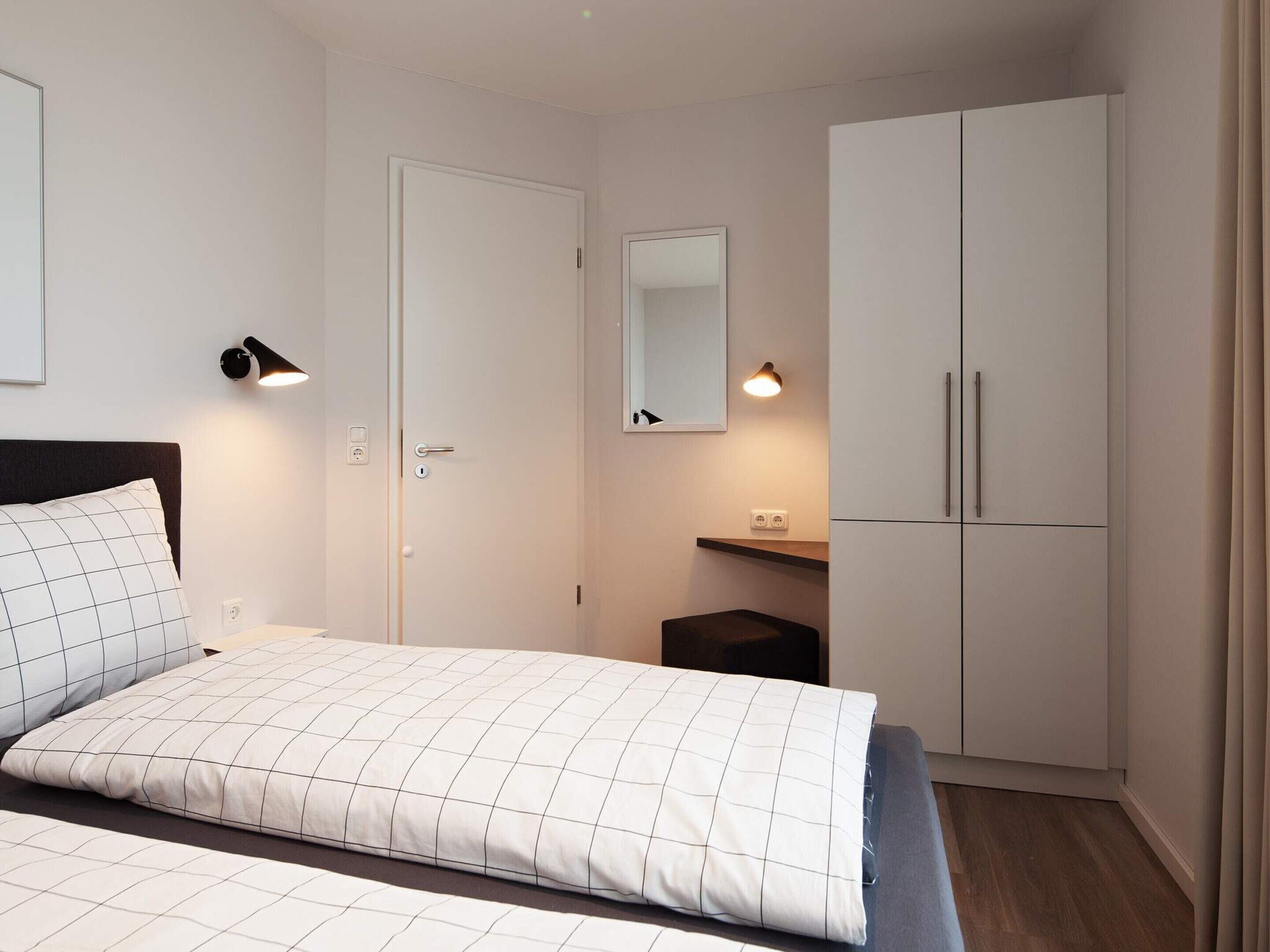 A bedroom with a bed, a wardrobe, a mirror, and a bedside lamp.
