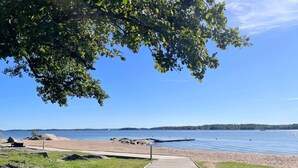 A wooden boardwalk leading to a sandy beach with a calm lake and distant shoreline. - 4 Star Holiday Home in Akersberga (Akersberga)