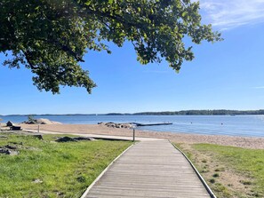 Pasarela de madera que conduce a una playa arenosa con un lago tranquilo y una costa distante.