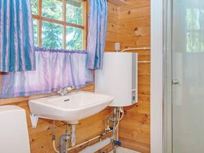 A bathroom with wooden walls, a window with curtains, a white sink, and a water heater.