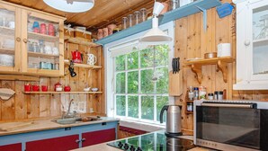A kitchen with wooden cabinets, a stainless steel kettle, a stove, and a window with a view of greenery. - 7 Person Holiday Home in Ebeltoft (Ebeltoft)