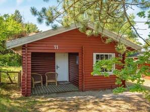 A small, red log cabin with the number 11, two wicker chairs outside, and a porch.