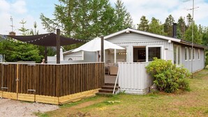 A single-story cabin with a covered patio, a fenced yard, and a chimney. - 9 Person Holiday Home in Vaeggerlose (Vaeggerlose)