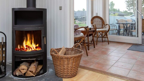A cozy room with a wood-burning stove, wicker basket, and wicker chairs. - 9 Person Holiday Home in Vaeggerlose (Vaeggerlose)