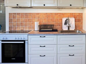 A kitchen with white cabinets, a Bosch oven, a sink with a faucet, and a backsplash with orange tiles. - 4 Star Holiday Home in Onsala (Gottskar)