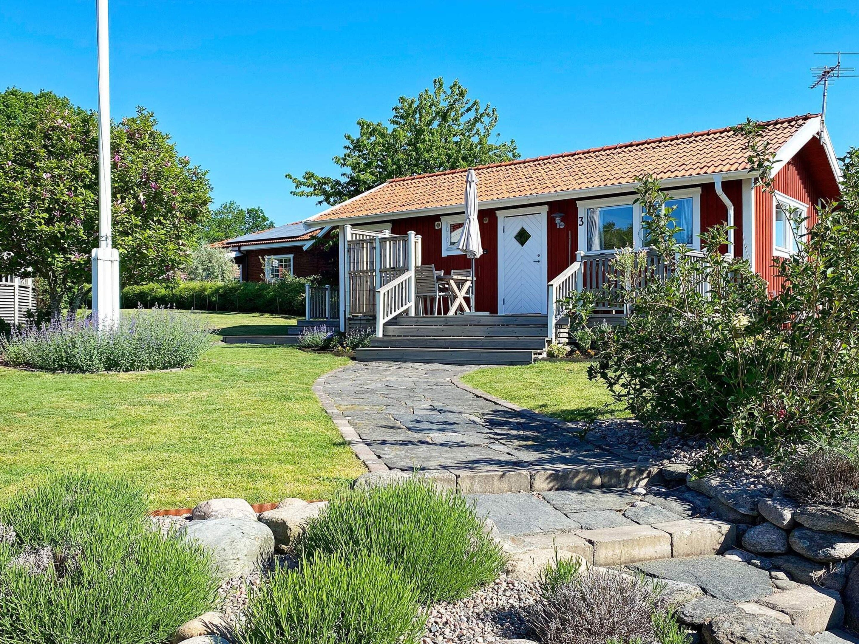 A red building with a tiled roof, a stone pathway leading to the entrance, and a well-maintained lawn.