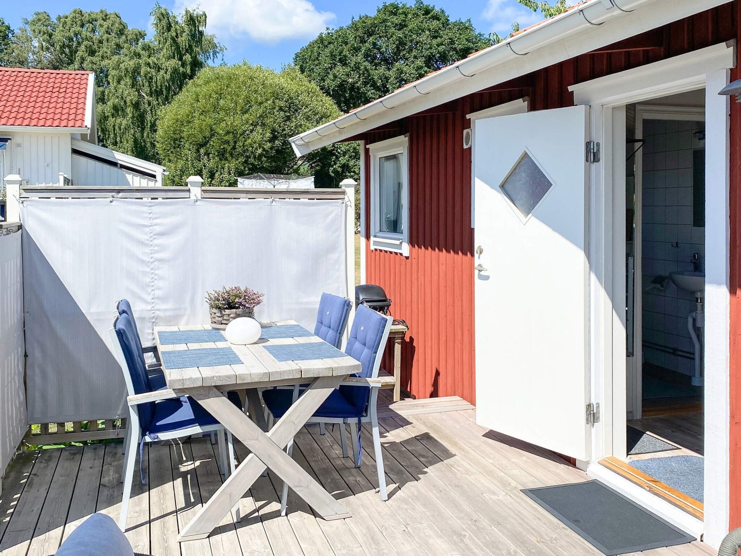 A wooden deck with a table and chairs, a barbecue grill, and a covered area with a white fence.