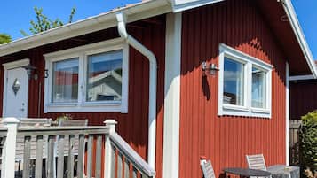 A red building with a white door, a window, and a small outdoor seating area with a table and chairs.