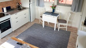 Kompakti keittiö, jossa on Bosch-uuni, jääkaappi, mikroaaltouuni sekä ruokailutila pöydän ja tuolien kera.