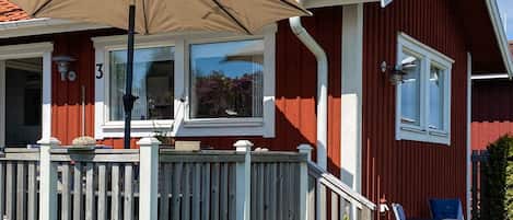 Un bâtiment rouge avec un cadre de fenêtre blanc, une terrasse en bois et une table avec des chaises.