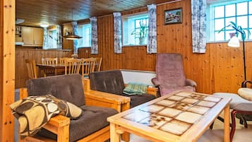 Interior acogedor de una cabaña con paredes de madera, un comedor y una zona de estar con mesa y sillas.