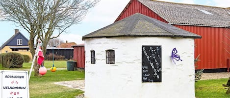 A small white building with a blackboard, surrounded by grass and a red barn in the background.