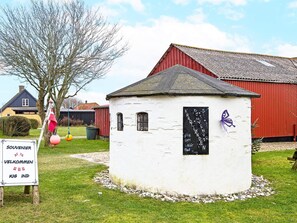 A small white building with a blackboard, surrounded by grass and a red barn in the background.