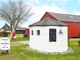 A small white building with a blackboard, surrounded by grass and a red barn in the background.