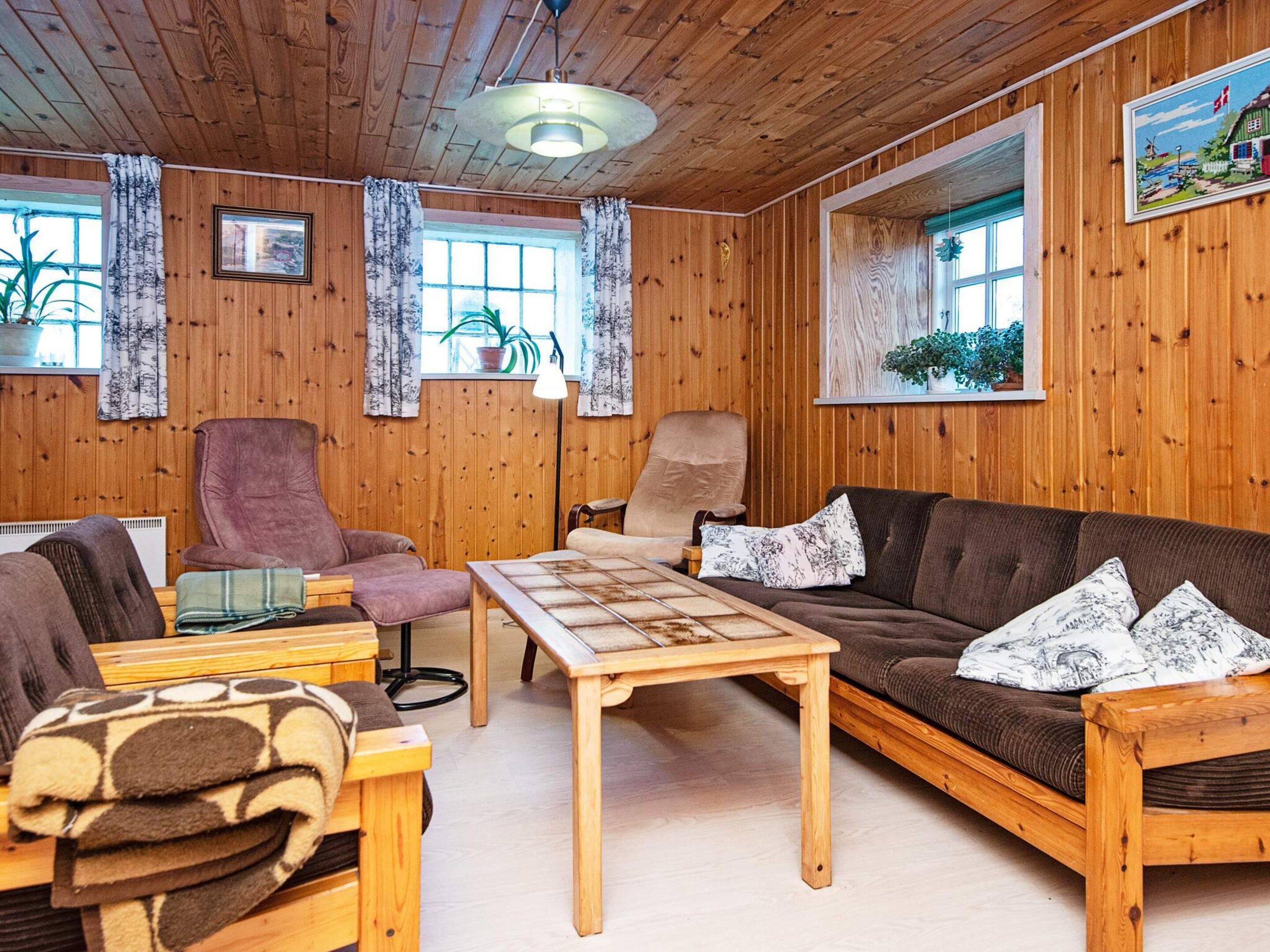 Une pièce chaleureuse avec des murs en bois, un canapé marron, une table basse en bois et deux fauteuils.