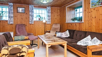 A cozy room with wooden walls, a brown sofa, a wooden coffee table, and two armchairs.