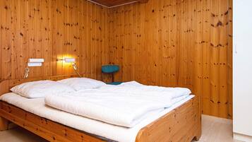 Una habitación con paneles de madera, una cama individual, una lámpara de pared y una silla.