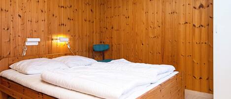 A wooden-paneled room with a single bed, a wall-mounted lamp, and a chair.