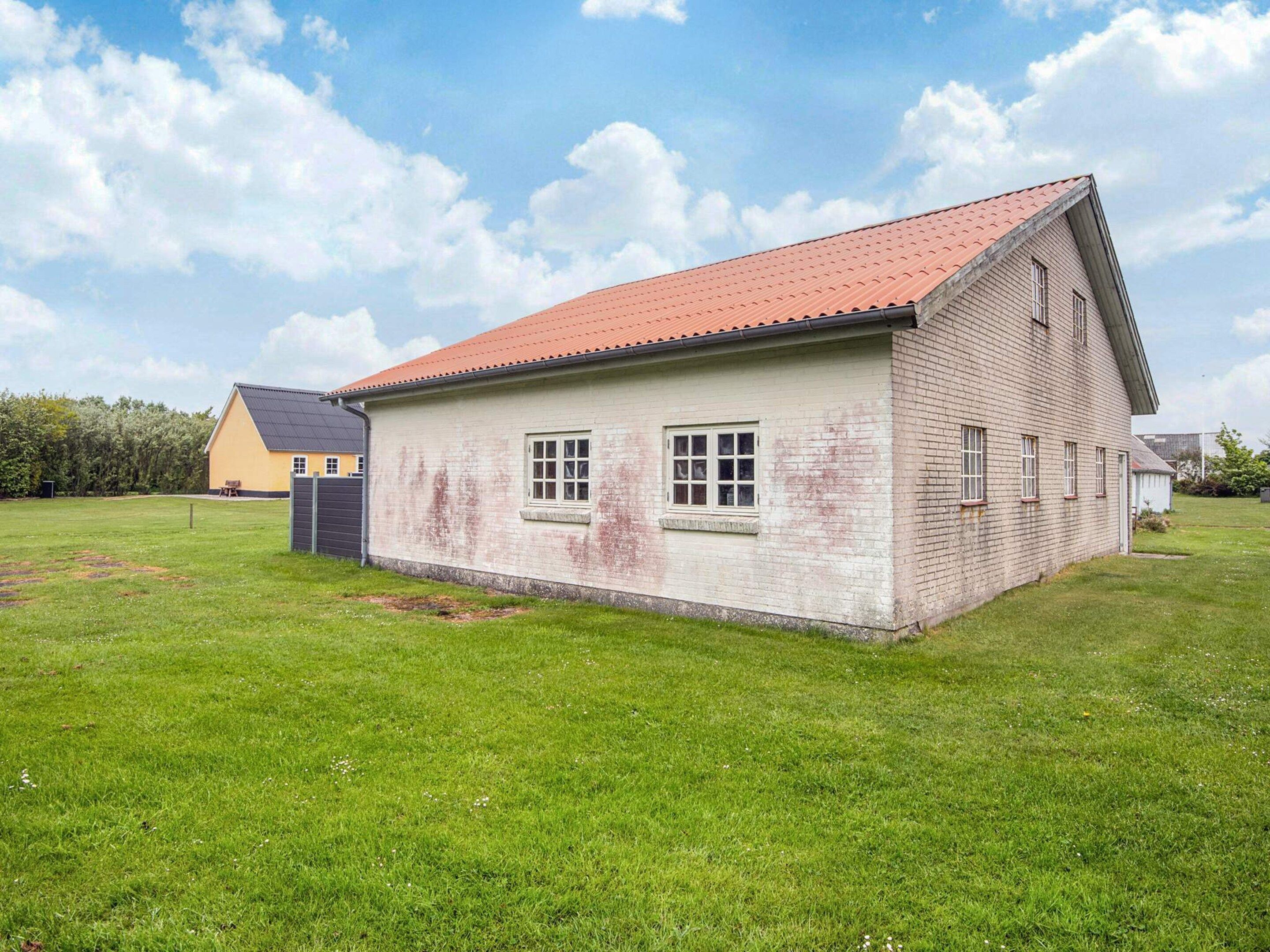 A single-story building with a red roof, a small porch, and a grassy yard.
